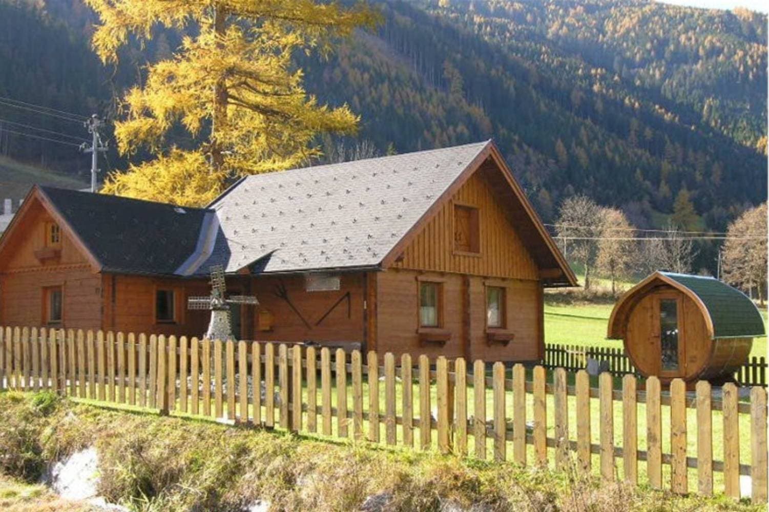 Fasssauna vor einem Holzhaus in herbstlicher Landschaft