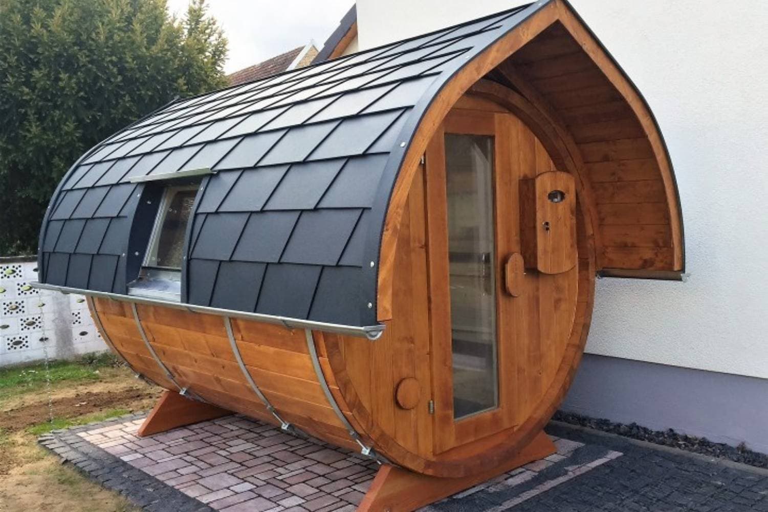 Fasssauna aus Holz mit dunklem Dach und kleinem Vorbau