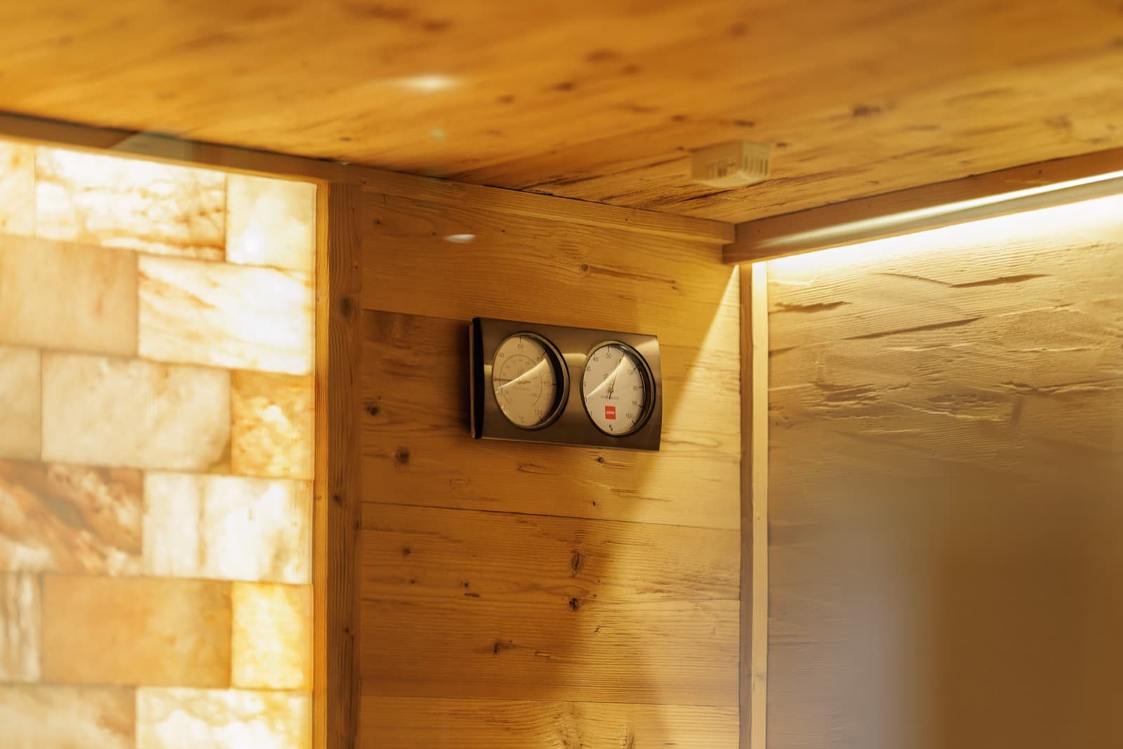 Thermometer und Hygrometer an der Holzwand einer Saunakabine, links eine beleuchtete Salzsteinwand.