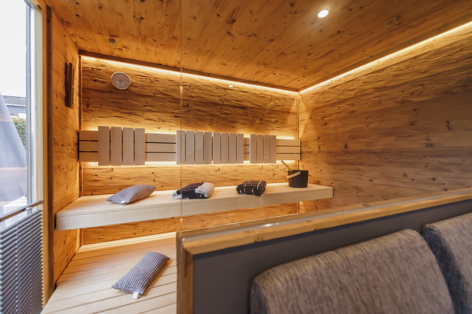 Saunaraum hinter einer Glaswand: zwei helle Holzbänke mit Rückenlehne, indirekte warmweiße LED-Lichtlinien an Decke, Rückenlehne und unter der Bank.