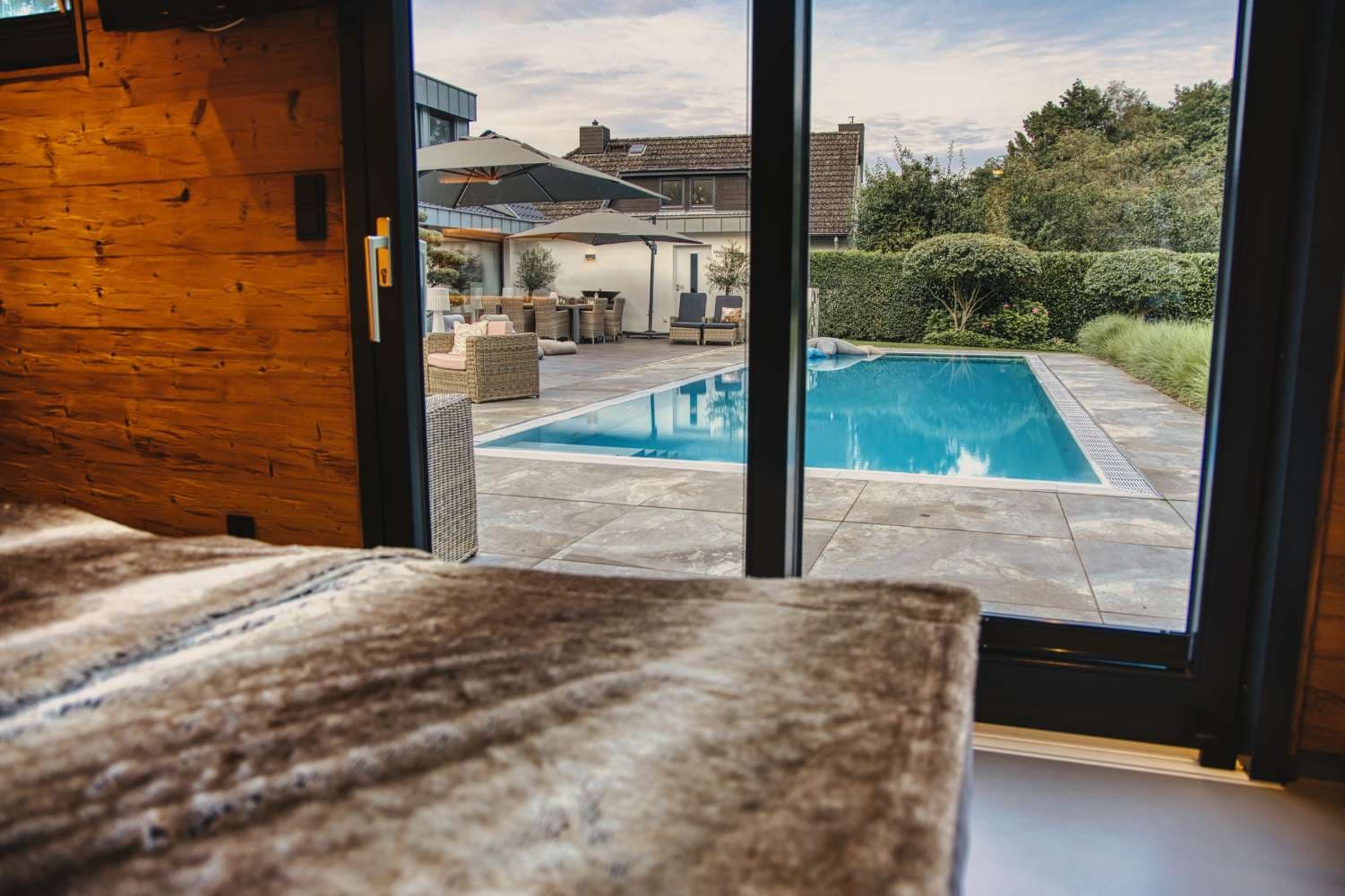 Ruheplatz im Holzinterieur mit Blick durch die Glastür auf Pool und Garten