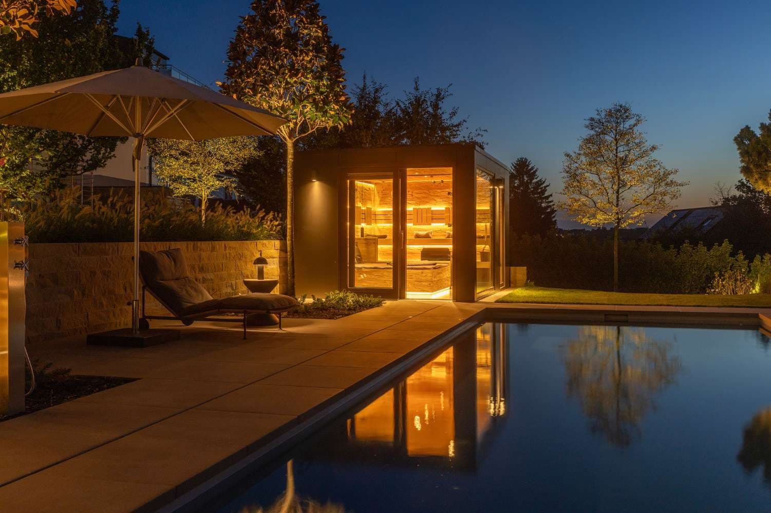 Beleuchtetes Spa-Haus mit Glasflächen neben einem Pool am Abend
