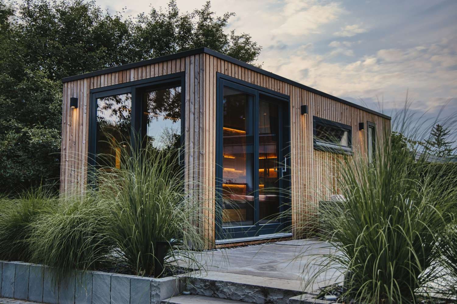Gartensauna mit Holzfassade und großen Glastüren zwischen Ziergräsern
